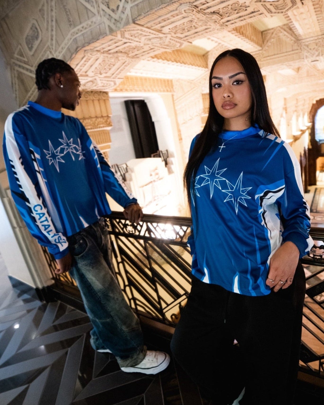 Two people wearing blue sports jerseys in an ornate indoor setting