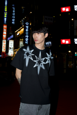 Person wearing a black t-shirt with white star design in an urban night setting with illuminated signs.