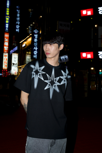 Person wearing a black t-shirt with white star design in an urban night setting with illuminated signs.